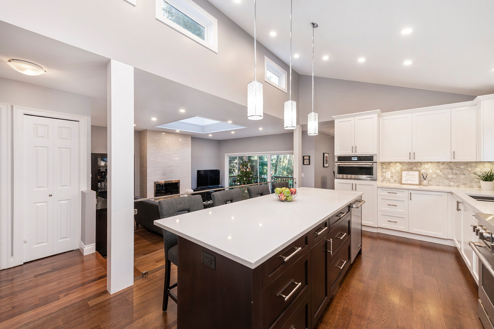 Example of a large transitional l-shaped medium tone wood floor and brown floor eat-in kitchen design in Vancouver with an undermount sink, shaker cabinets, white cabinets, quartzite countertops, multicolored backsplash, marble backsplash, stainless steel appliances, an island and white countertops