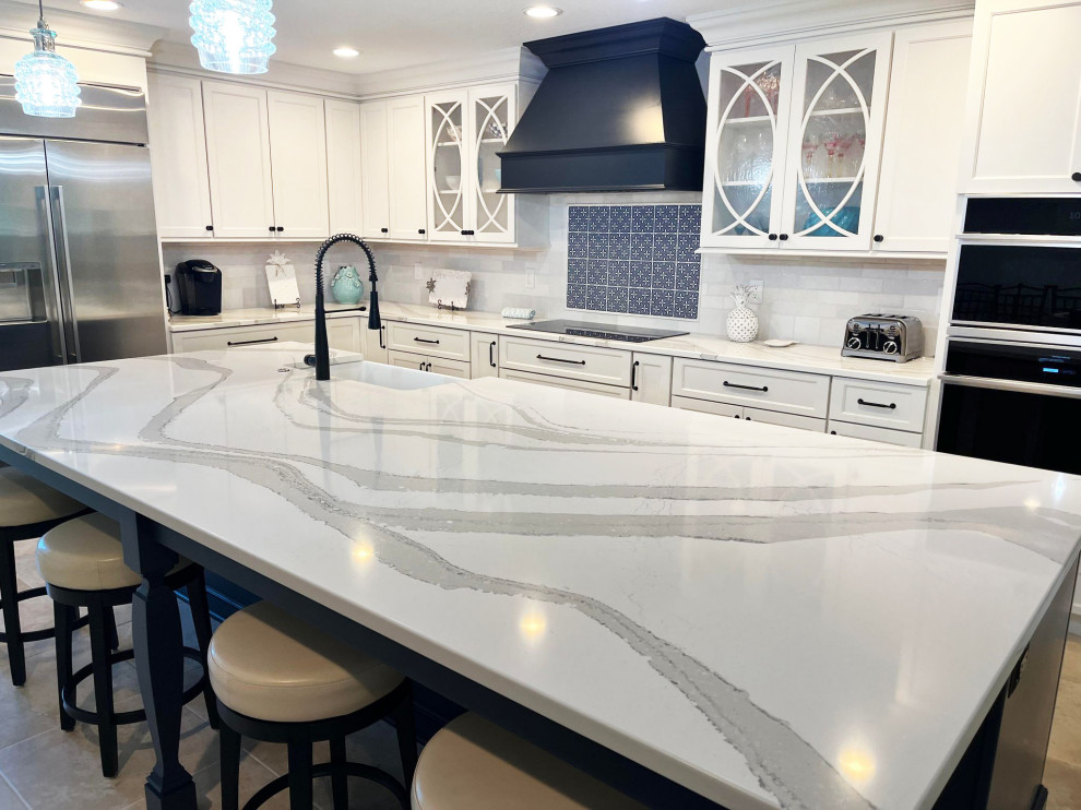 Example of a transitional l-shaped eat-in kitchen design with an undermount sink, shaker cabinets, white cabinets, quartz countertops, white backsplash, subway tile backsplash, stainless steel appliances, an island and multicolored countertops