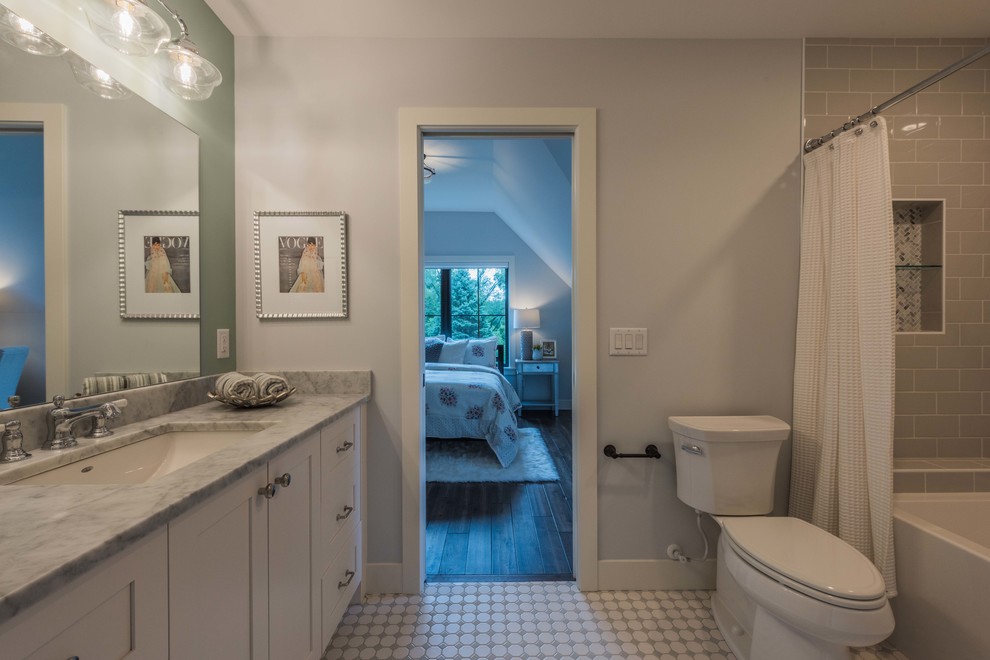 Design ideas for a mid-sized country kids bathroom in Minneapolis with shaker cabinets, white cabinets, an alcove tub, a shower/bathtub combo, a two-piece toilet, gray tile, cement tile, grey walls, ceramic floors, an undermount sink, marble benchtops, white floor, a shower curtain and grey benchtops.
