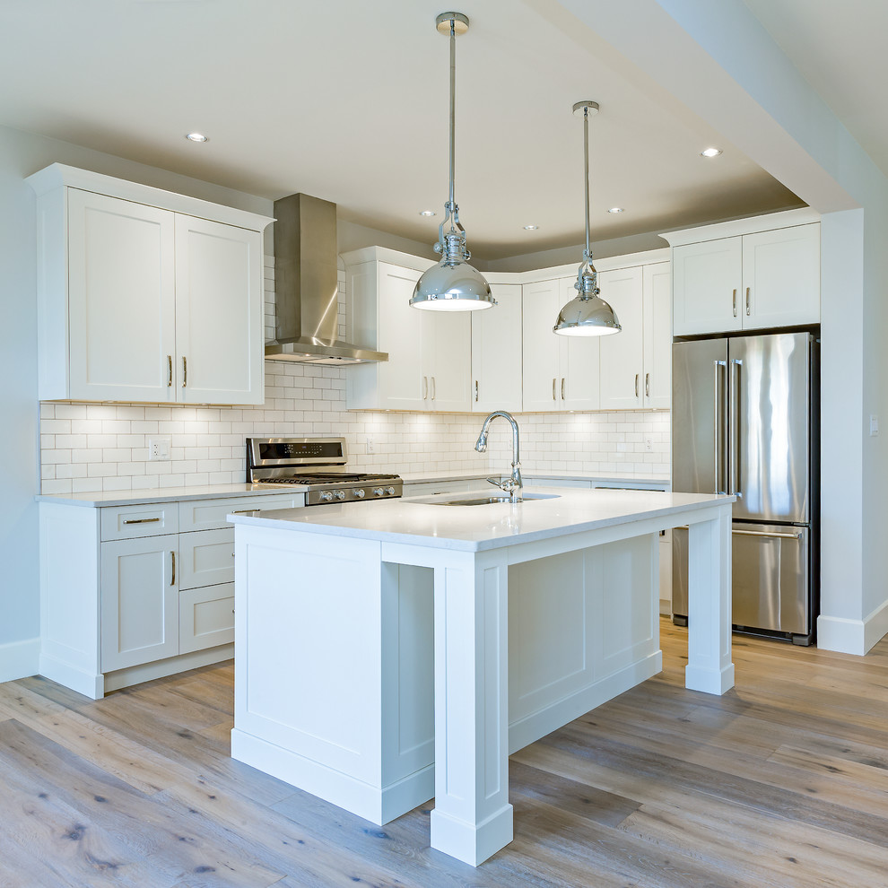 Open concept kitchen - mid-sized transitional l-shaped light wood floor open concept kitchen idea with an undermount sink, shaker cabinets, white cabinets, quartz countertops, white backsplash, subway tile backsplash, stainless steel appliances, an island and white countertops