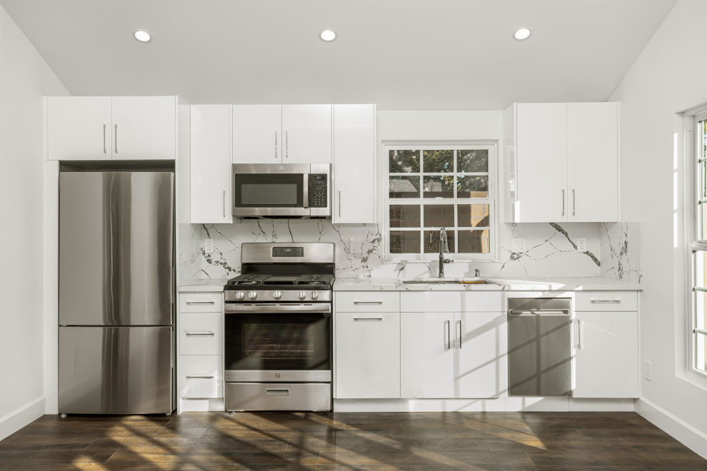Bild på ett litet vintage vit linjärt vitt kök med öppen planlösning, med en undermonterad diskho, släta luckor, vita skåp, bänkskiva i kvarts, vitt stänkskydd, rostfria vitvaror, laminatgolv och brunt golv
