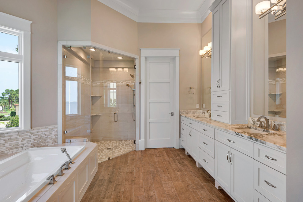 Expansive transitional master bathroom in Miami with shaker cabinets, white cabinets, an alcove tub, a corner shower, a one-piece toilet, beige tile, matchstick tile, beige walls, medium hardwood floors, an undermount sink, marble benchtops, beige floor and a hinged shower door.