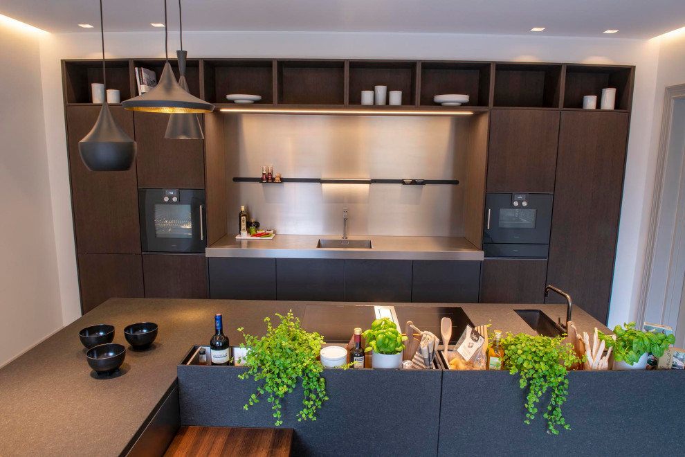 This is an example of a large modern open plan kitchen in Other with a single-bowl sink, flat-panel cabinets, dark wood cabinets, granite worktops, metallic splashback, black appliances, ceramic flooring, an island, grey floors and black worktops.