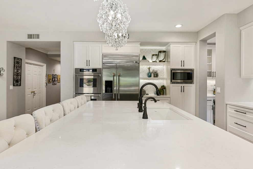 Huge transitional u-shaped travertine floor and beige floor open concept kitchen photo in Orange County with a single-bowl sink, shaker cabinets, white cabinets, quartz countertops, multicolored backsplash, stone tile backsplash, stainless steel appliances, an island and white countertops