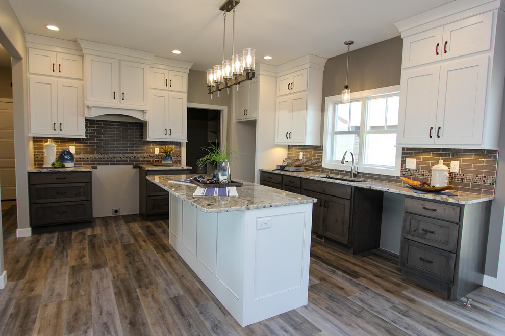 Example of a mid-sized transitional l-shaped laminate floor and brown floor eat-in kitchen design in Minneapolis with an undermount sink, shaker cabinets, white cabinets, granite countertops, gray backsplash, ceramic backsplash, an island and multicolored countertops