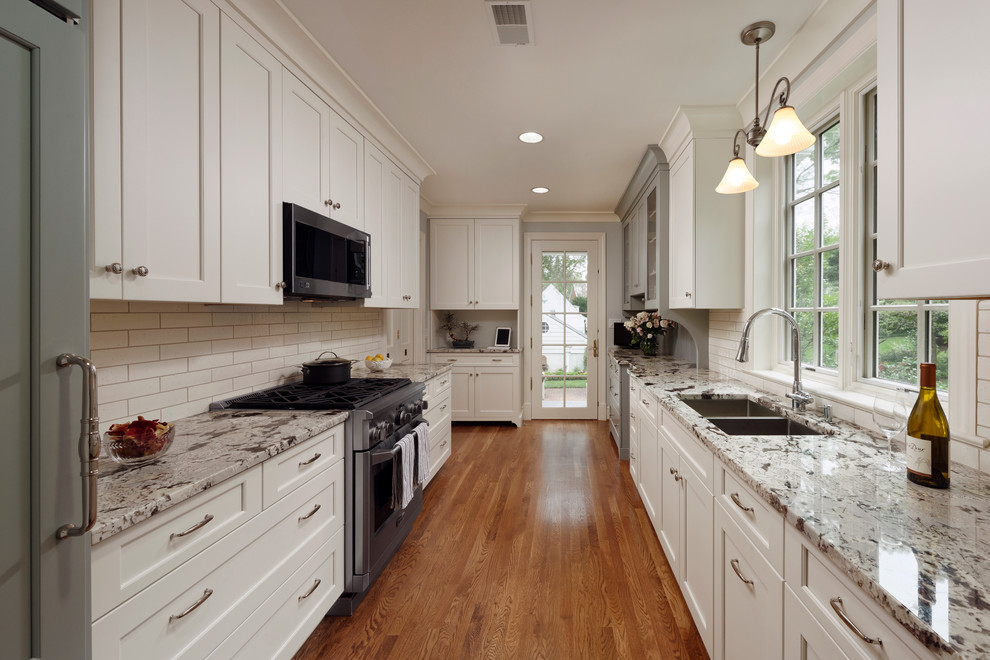 Inspiration for a small transitional galley eat-in kitchen in DC Metro with a double-bowl sink, glass-front cabinets, white cabinets, granite benchtops, white splashback, glass tile splashback, stainless steel appliances, light hardwood floors, no island and beige floor.