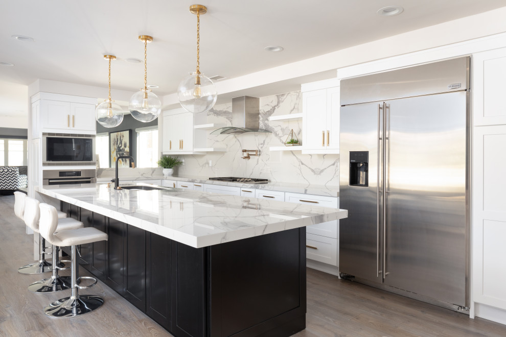 Design ideas for a medium sized contemporary l-shaped open plan kitchen in Orange County with shaker cabinets, white cabinets, white splashback, porcelain splashback, stainless steel appliances, light hardwood flooring, an island, brown floors and white worktops.