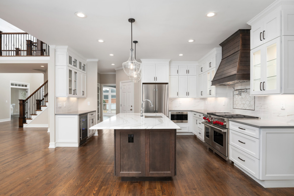 Inspiration for a large transitional l-shaped open plan kitchen in Atlanta with a double-bowl sink, shaker cabinets, white cabinets, quartz benchtops, white splashback, subway tile splashback, stainless steel appliances, dark hardwood floors, with island, brown floor and white benchtop.