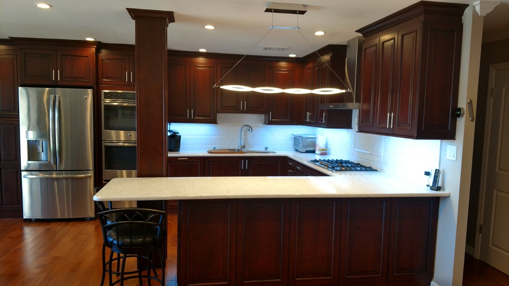 Inspiration for a large transitional u-shaped medium tone wood floor kitchen remodel in New York with an undermount sink, raised-panel cabinets, dark wood cabinets, white backsplash, subway tile backsplash, stainless steel appliances and a peninsula