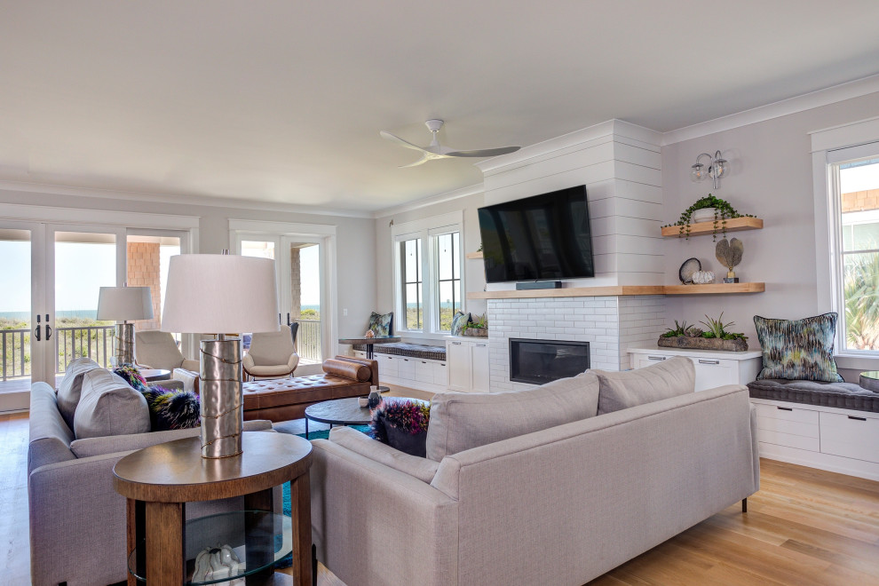 Photo of an expansive beach style open concept living room in Wilmington with white walls, medium hardwood floors, a standard fireplace, a tile fireplace surround, a wall-mounted tv, brown floor and planked wall panelling.