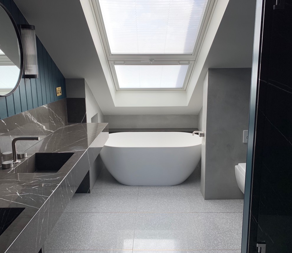 This is an example of a small scandinavian master bathroom in London with open cabinets, grey cabinets, a freestanding tub, an open shower, a wall-mount toilet, gray tile, limestone, blue walls, terrazzo floors, an undermount sink, marble benchtops, grey floor, a hinged shower door and grey benchtops.