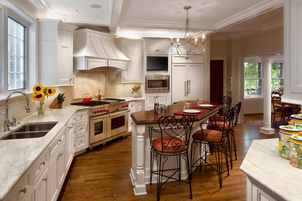 This is an example of a large traditional l-shaped eat-in kitchen in Cleveland with an undermount sink, beaded inset cabinets, white cabinets, wood benchtops, beige splashback, porcelain splashback, stainless steel appliances, dark hardwood floors, with island and beige floor.