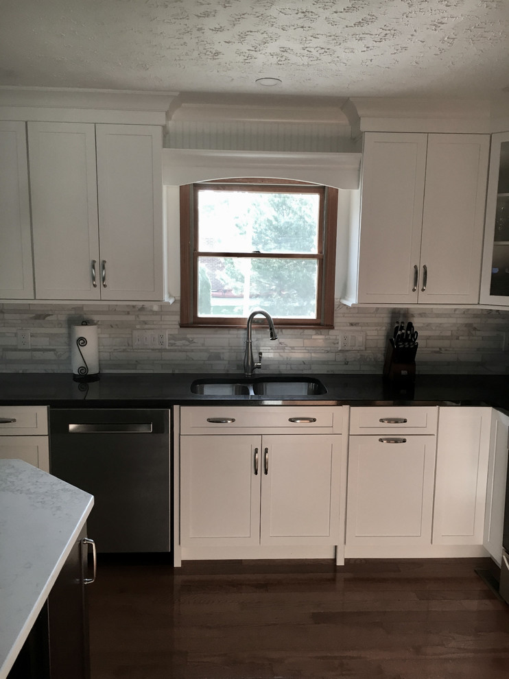 Example of a large transitional single-wall medium tone wood floor eat-in kitchen design with an undermount sink, shaker cabinets, white cabinets, granite countertops, multicolored backsplash, marble backsplash, stainless steel appliances, an island and black countertops