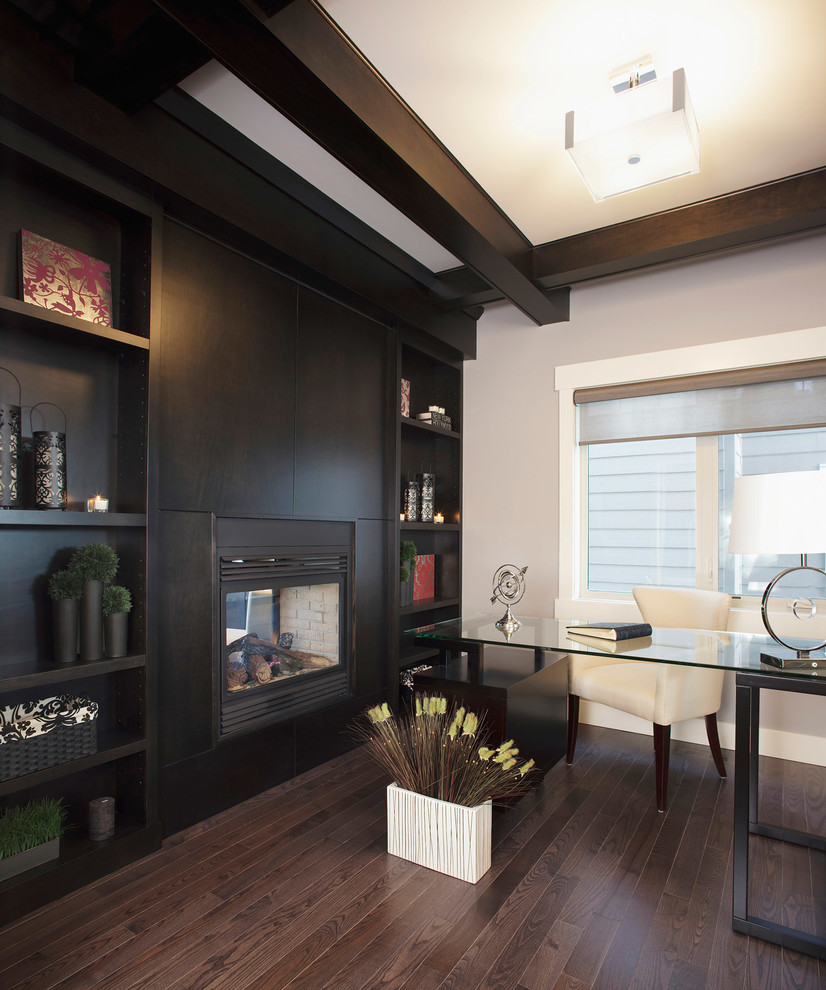 Photo of a transitional study room in Calgary with grey walls, dark hardwood floors, a two-sided fireplace, a wood fireplace surround and a freestanding desk.