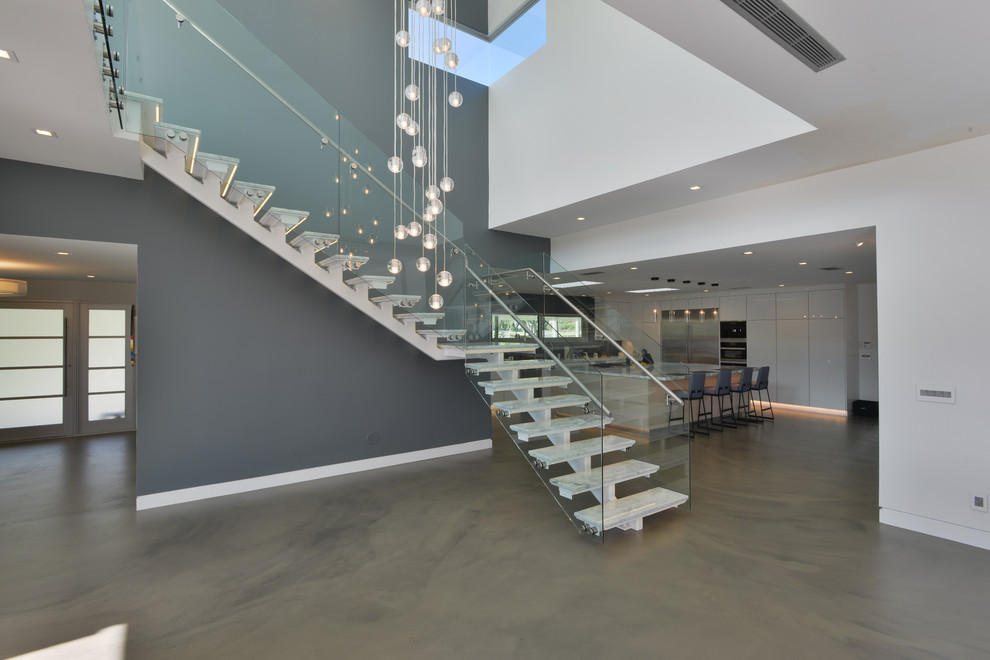 Design ideas for a mid-sized modern marble l-shaped staircase in Los Angeles with open risers and glass railing.