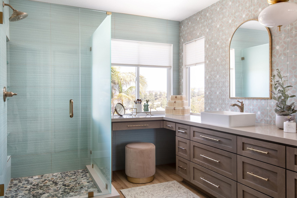 На фото: ванная комната среднего размера в морском стиле с фасадами в стиле шейкер, угловым душем, синей плиткой, керамогранитной плиткой, синими стенами, полом из ламината, настольной раковиной, столешницей из искусственного кварца, коричневым полом, душем с распашными дверями, синей столешницей, тумбой под две раковины и встроенной тумбой
