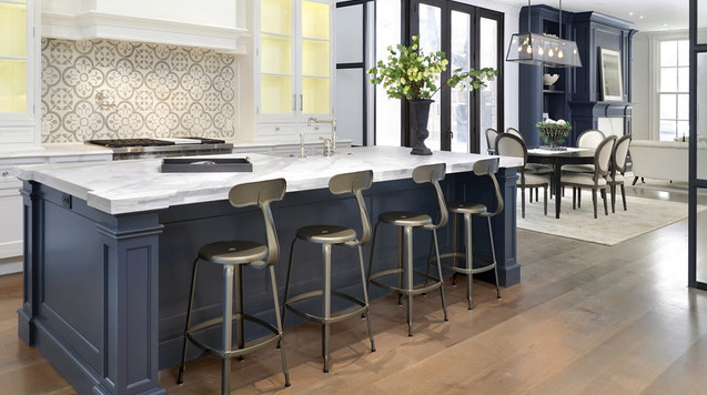 Mid-sized transitional l-shaped medium tone wood floor open concept kitchen photo in Chicago with a farmhouse sink, recessed-panel cabinets, white cabinets, marble countertops, white backsplash, mosaic tile backsplash, stainless steel appliances and an island