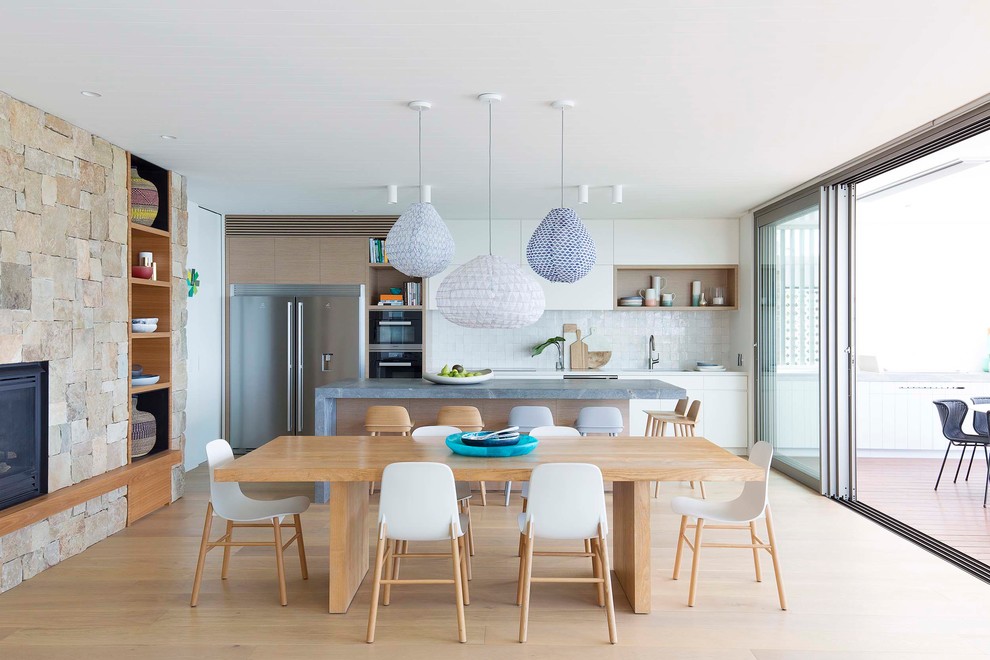 Inspiration for a large beach style galley open plan kitchen in Sydney with an undermount sink, flat-panel cabinets, white cabinets, quartz benchtops, white splashback, ceramic splashback, stainless steel appliances, light hardwood floors and with island.