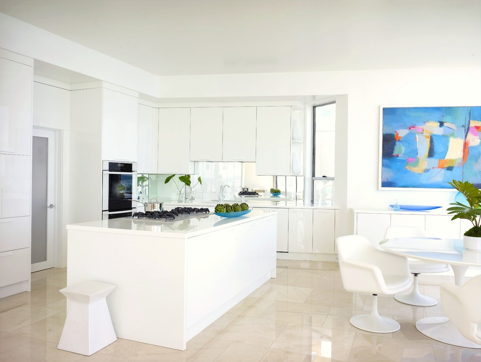 This is an example of a beach style l-shaped eat-in kitchen in Los Angeles with flat-panel cabinets, white cabinets, mirror splashback, with island and beige floor.