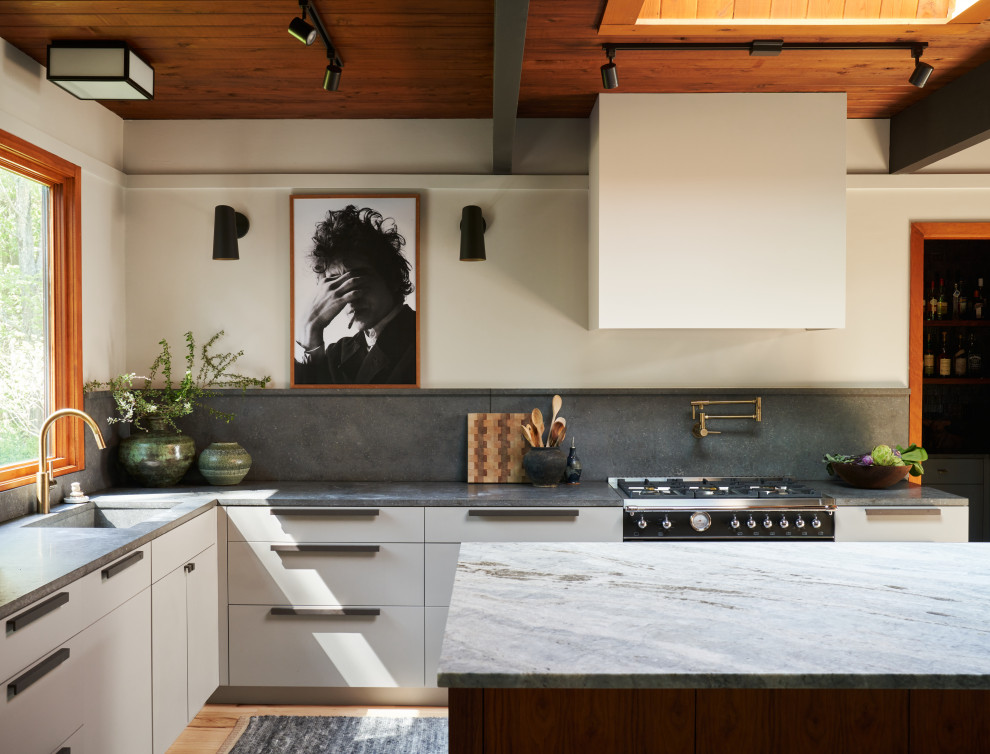 Inredning av ett 60 tals mellanstort grå grått kök, med en undermonterad diskho, marmorbänkskiva, grått stänkskydd, ljust trägolv, en köksö, brunt golv, släta luckor, vita skåp och rostfria vitvaror