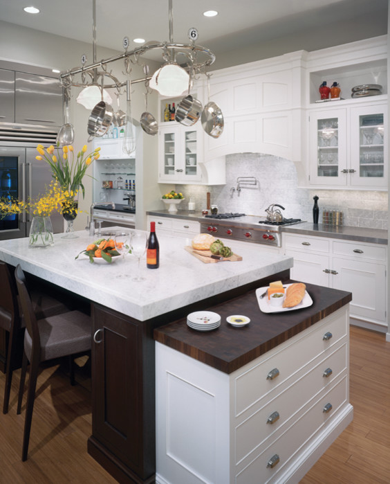 Design ideas for a large traditional l-shaped eat-in kitchen in Seattle with a triple-bowl sink, glass-front cabinets, white cabinets, white splashback, ceramic splashback, stainless steel appliances, light hardwood floors, with island, marble benchtops and brown floor.