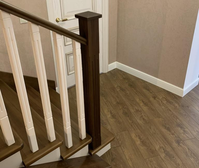 Лестница с темными ступенями под цвет паркета и белыми балясинами.