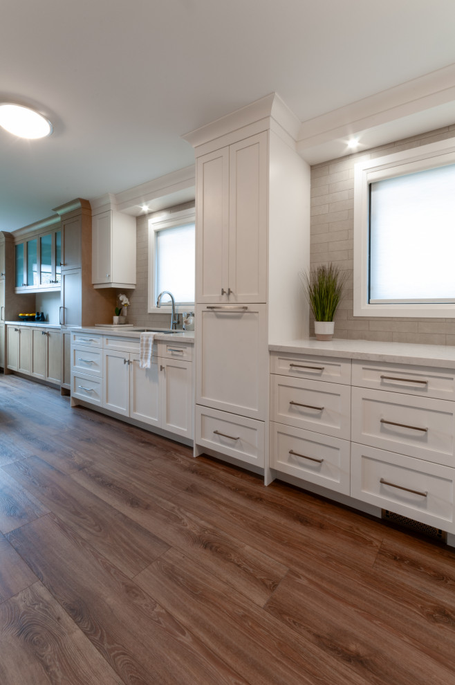 Inspiration for a mid-sized transitional galley laminate floor and brown floor eat-in kitchen remodel in Toronto with an undermount sink, recessed-panel cabinets, white cabinets, quartz countertops, beige backsplash, porcelain backsplash, stainless steel appliances and yellow countertops