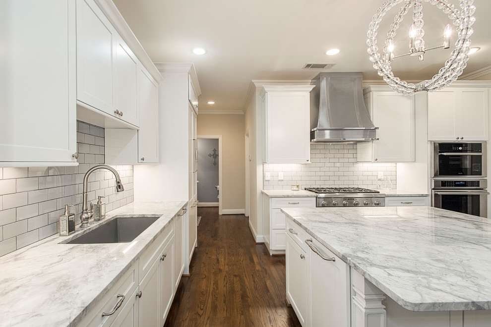 Open concept kitchen - large transitional u-shaped medium tone wood floor open concept kitchen idea in Dallas with an undermount sink, shaker cabinets, white cabinets, quartz countertops, white backsplash, porcelain backsplash, stainless steel appliances and an island