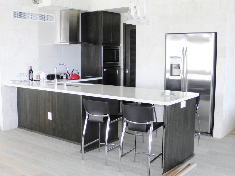 Small asian l-shaped eat-in kitchen in Hawaii with an undermount sink, flat-panel cabinets, black cabinets, solid surface benchtops, grey splashback, ceramic splashback, stainless steel appliances, light hardwood floors, a peninsula and grey floor.