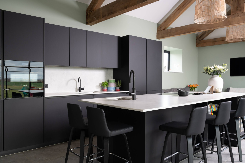 Medium sized contemporary galley open plan kitchen in Hertfordshire with a single-bowl sink, flat-panel cabinets, black cabinets, concrete worktops, white splashback, integrated appliances, an island, grey floors, white worktops, concrete flooring, exposed beams and a vaulted ceiling.