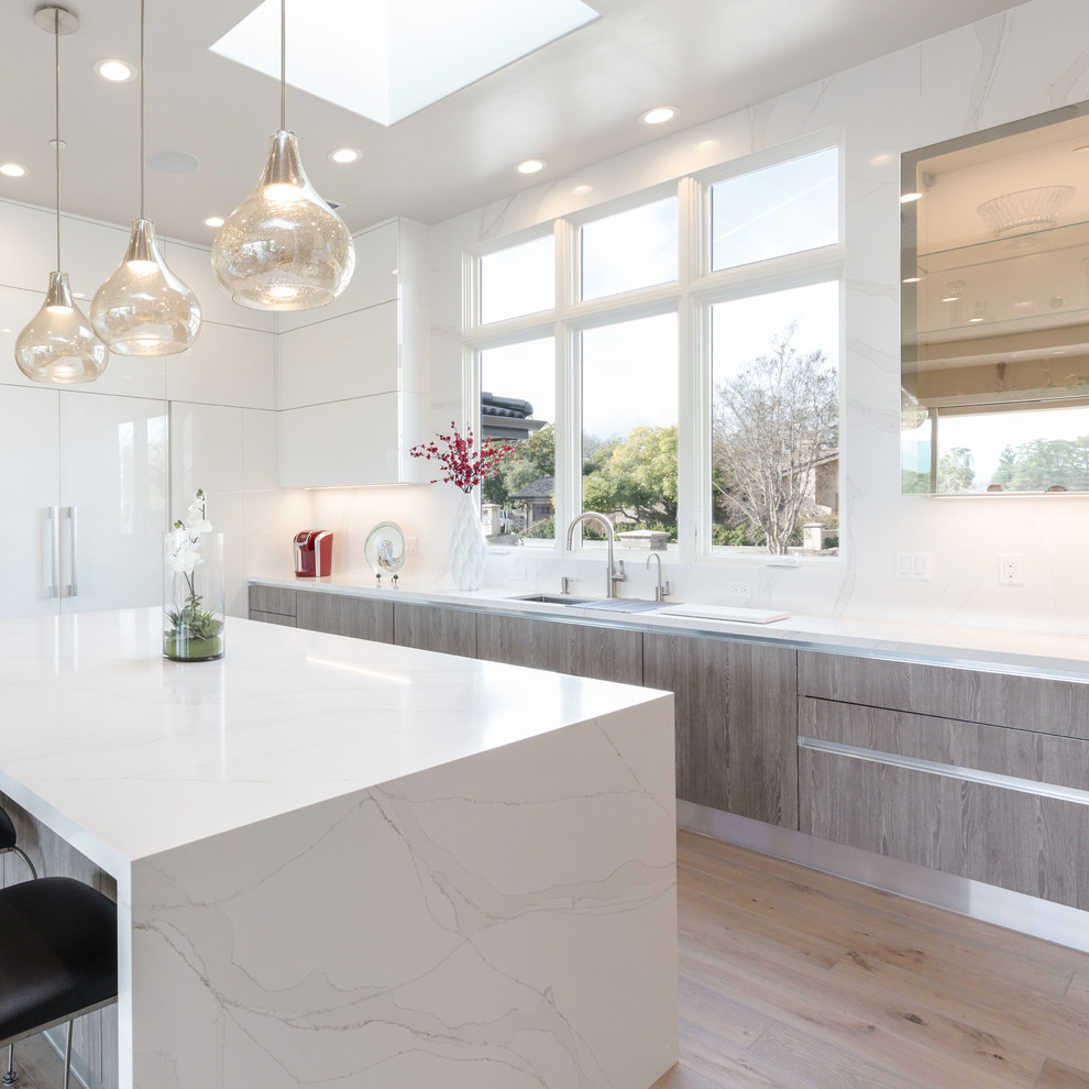 Design ideas for a large modern u-shaped open plan kitchen in San Francisco with an undermount sink, flat-panel cabinets, white cabinets, quartz benchtops, white splashback, stone slab splashback, stainless steel appliances, light hardwood floors, with island and brown floor.