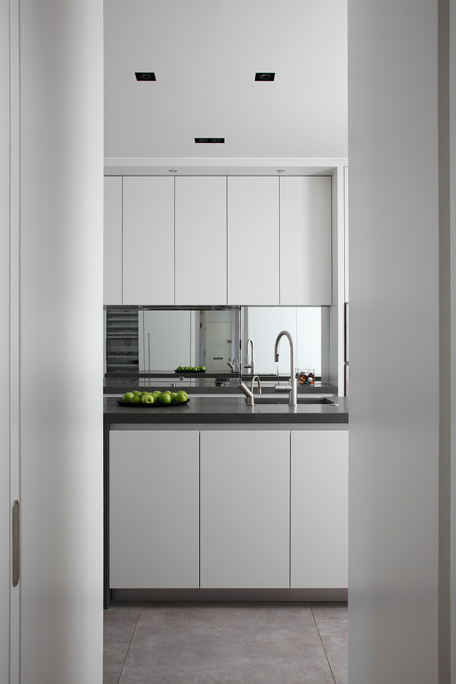 Design ideas for a mid-sized contemporary single-wall separate kitchen in London with an undermount sink, flat-panel cabinets, white cabinets, marble benchtops, metallic splashback, glass sheet splashback, stainless steel appliances, porcelain floors, with island, brown floor and grey benchtop.