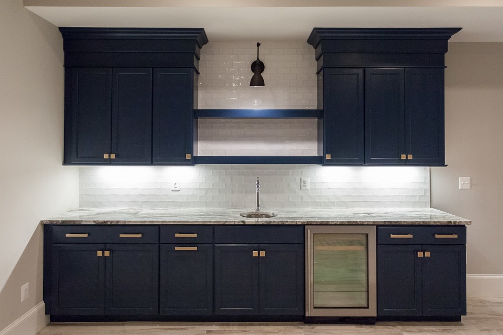 Large contemporary single-wall eat-in kitchen in DC Metro with a farmhouse sink, shaker cabinets, blue cabinets, granite benchtops, white splashback, porcelain splashback, stainless steel appliances, medium hardwood floors, with island, white floor and grey benchtop.