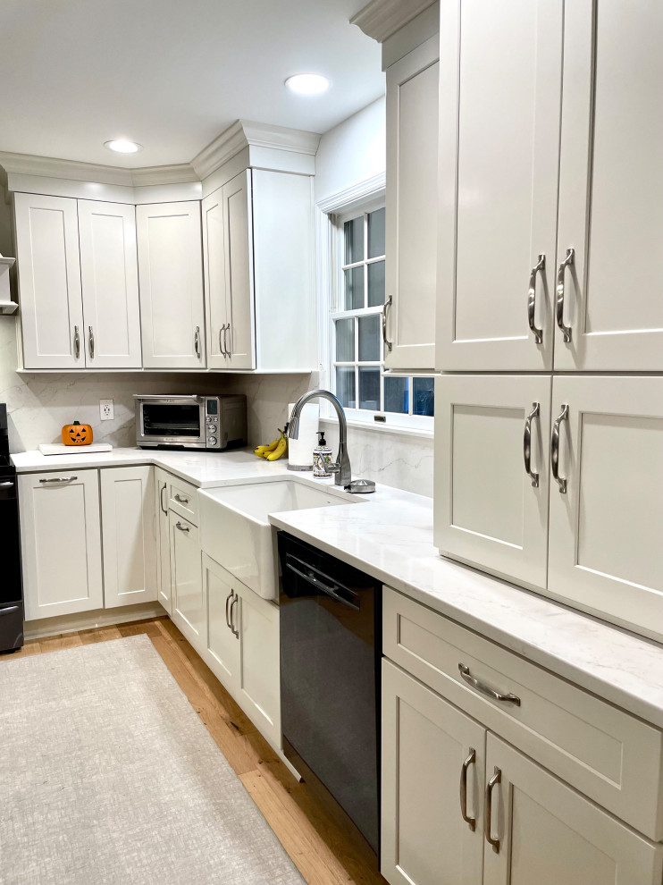 Inspiration for a transitional l-shaped light wood floor and beige floor eat-in kitchen remodel with a farmhouse sink, shaker cabinets, white cabinets, quartz countertops, white backsplash, quartz backsplash, black appliances, an island and white countertops