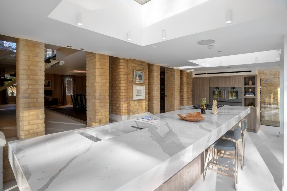 Inspiration for a large contemporary galley open plan kitchen in London with an undermount sink, flat-panel cabinets, light wood cabinets, quartzite benchtops, panelled appliances, porcelain floors, white floor, with island and grey benchtop.