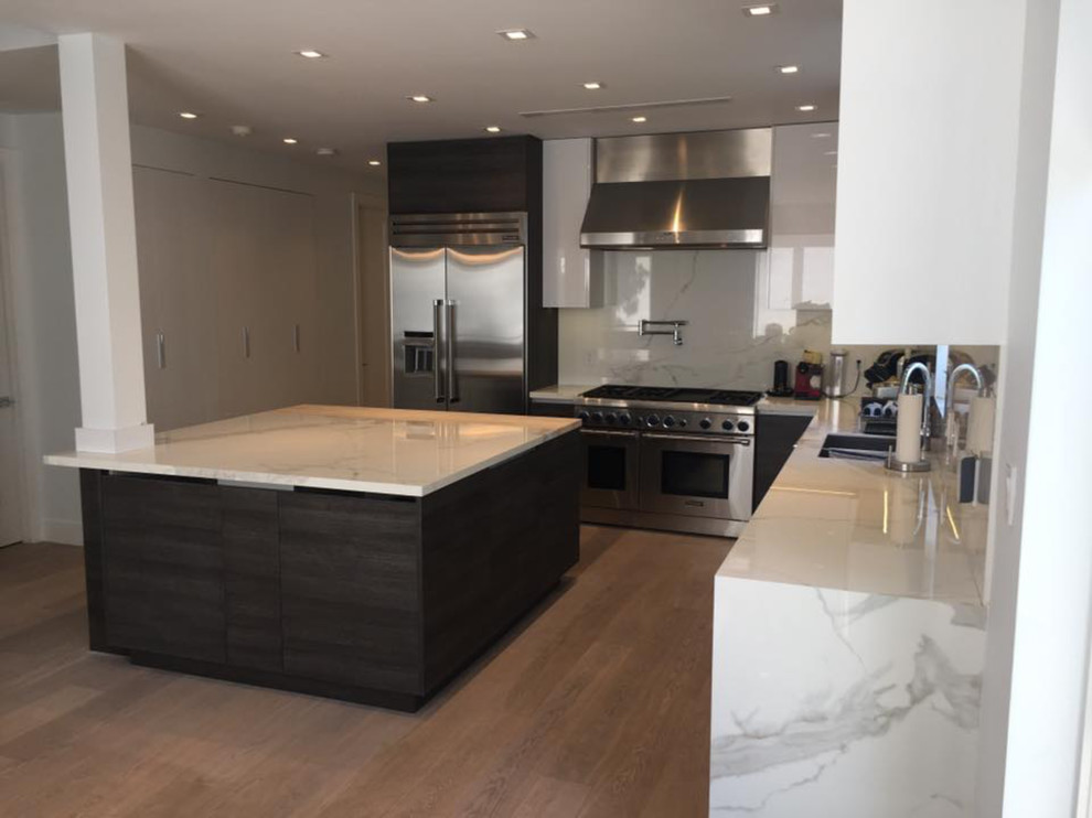 Large modern l-shaped kitchen in Miami with a double-bowl sink, flat-panel cabinets, black cabinets, marble benchtops, stone slab splashback, stainless steel appliances, light hardwood floors and with island.