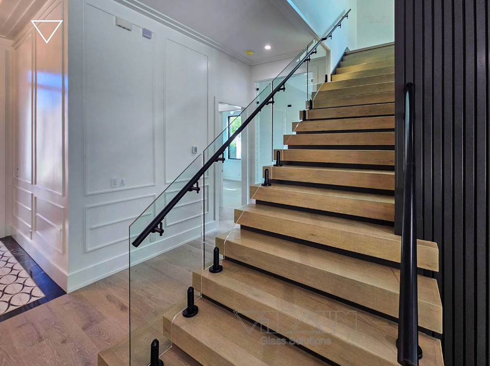 Ejemplo de escalera recta minimalista grande con escalones de vidrio, barandilla de metal y madera