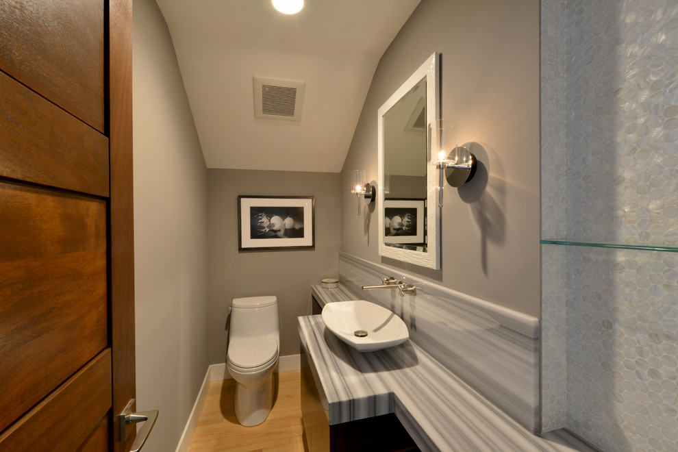 This is an example of a small contemporary powder room in San Diego with flat-panel cabinets, black cabinets, a one-piece toilet, grey walls, light hardwood floors, a vessel sink and onyx benchtops.