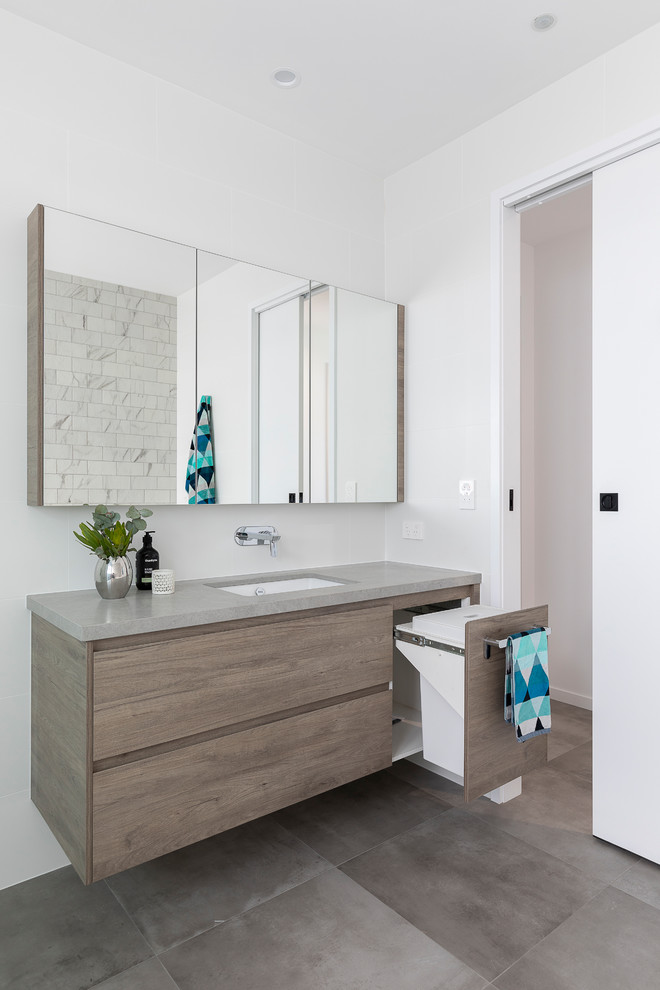 This is an example of a mid-sized contemporary 3/4 bathroom in Brisbane with furniture-like cabinets, medium wood cabinets, a corner tub, an open shower, a one-piece toilet, white tile, ceramic tile, white walls, cement tiles, an undermount sink, engineered quartz benchtops, grey floor, an open shower and grey benchtops.