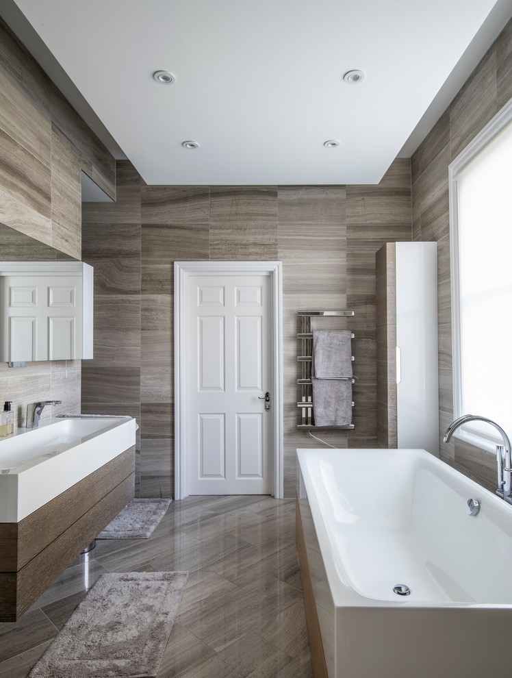 This is an example of a contemporary bathroom in London with flat-panel cabinets, a freestanding tub, brown tile, gray tile, a trough sink and dark wood cabinets.