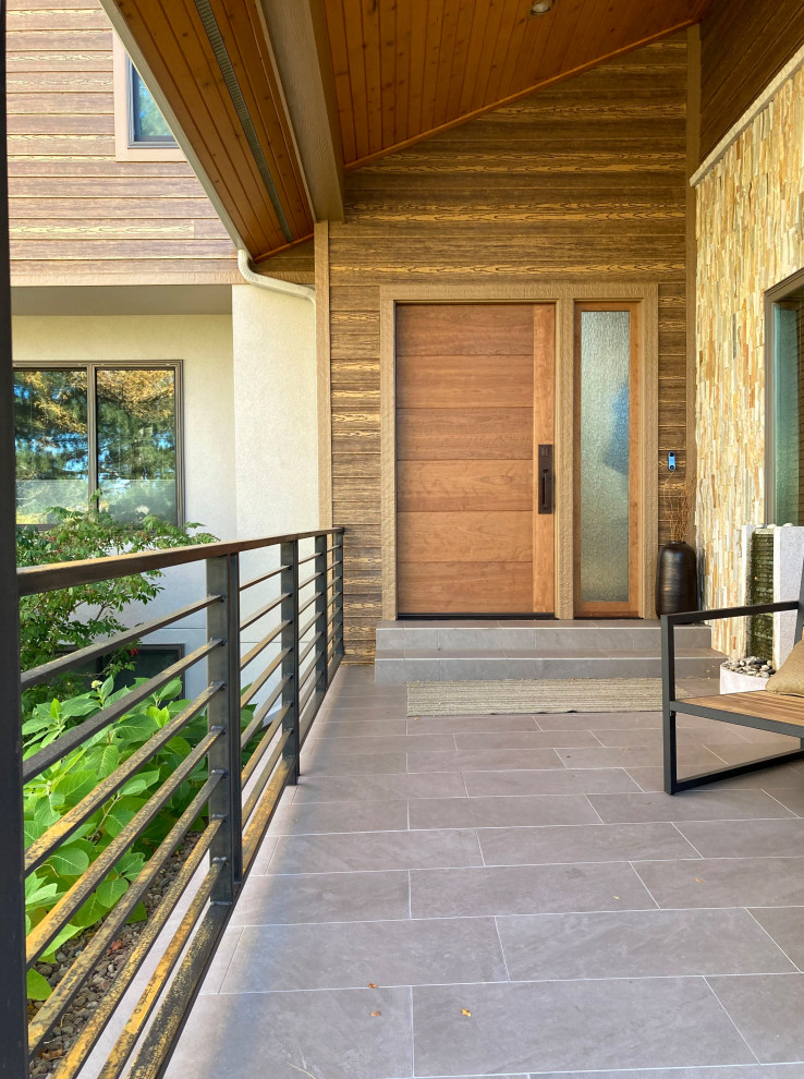 Immagine di un portico minimalista con piastrelle, un tetto a sbalzo e parapetto in metallo
