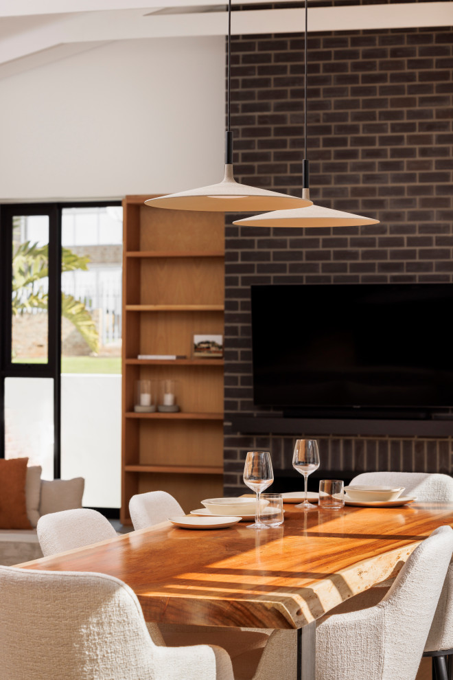 This is an example of a mid-sized modern open plan dining in Orange County with black walls, medium hardwood floors, a standard fireplace, a brick fireplace surround, beige floor, vaulted and brick walls.