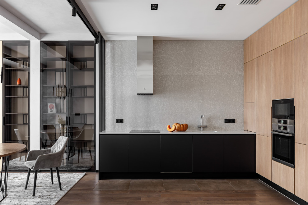This is an example of a contemporary l-shaped open plan kitchen in Saint Petersburg with an undermount sink, flat-panel cabinets, black cabinets, grey splashback, stainless steel appliances, no island, brown floor and white benchtop.