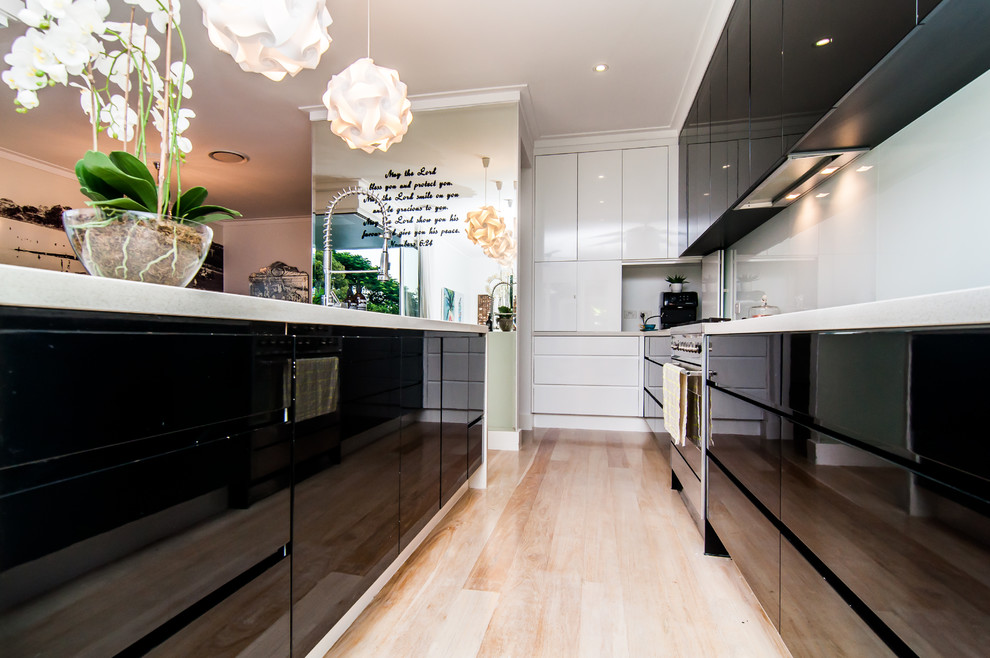Photo of a mid-sized contemporary galley open plan kitchen in Brisbane with white splashback, stainless steel appliances, light hardwood floors, with island, multi-coloured benchtop, a drop-in sink, shaker cabinets, brown cabinets and glass sheet splashback.