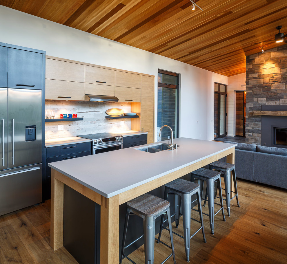Photo of a country open plan kitchen in Ottawa with a double-bowl sink, flat-panel cabinets, light wood cabinets, multi-coloured splashback, stainless steel appliances, medium hardwood floors, with island and white benchtop.