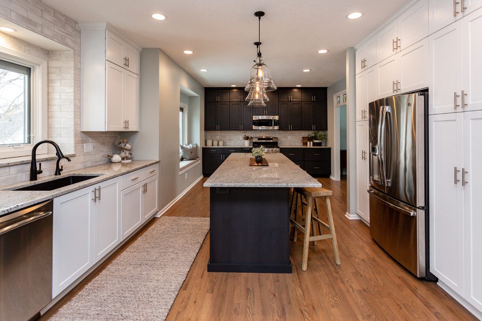 Example of a large transitional u-shaped medium tone wood floor and brown floor eat-in kitchen design with an undermount sink, recessed-panel cabinets, white cabinets, granite countertops, white backsplash, subway tile backsplash, stainless steel appliances, an island and gray countertops