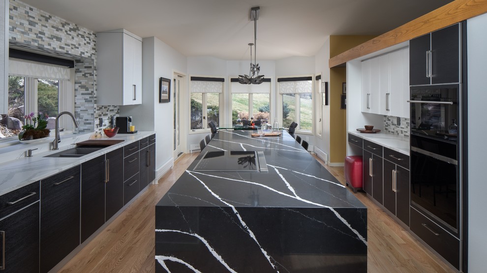 Inspiration for a large contemporary galley eat-in kitchen in Denver with an undermount sink, flat-panel cabinets, black cabinets, quartz benchtops, multi-coloured splashback, glass tile splashback, panelled appliances, light hardwood floors, with island, beige floor and black benchtop.