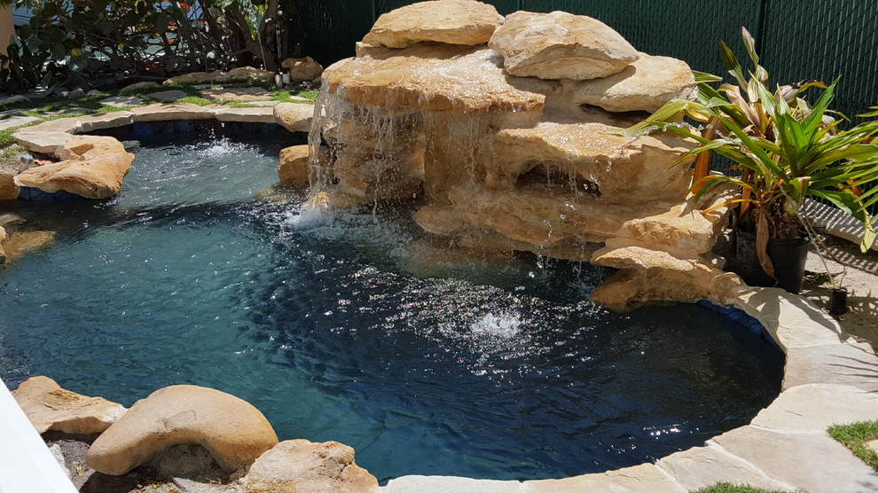 Inspiration for a small tropical backyard custom-shaped natural pool in Miami with a water feature and natural stone pavers.