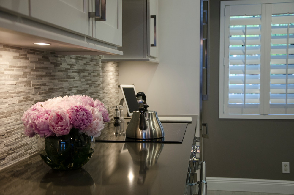 Kitchen - small transitional u-shaped porcelain tile kitchen idea in Miami with a farmhouse sink, shaker cabinets, white cabinets, quartz countertops, gray backsplash, stone tile backsplash, stainless steel appliances and no island