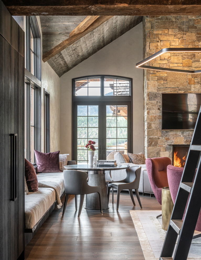 This is an example of a rustic dining room in Other with grey walls, dark hardwood flooring, a standard fireplace, a stone fireplace surround, brown floors, exposed beams, a vaulted ceiling and a wood ceiling.